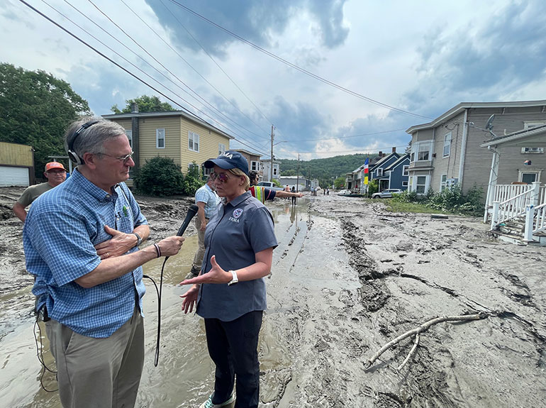 Photo: FEMA Administrator Deanne Criswell is interviewed by Vermont Public's Bob Kinzel in Barre on July 12, on a tour of flooding destruction with Governor Scott and the Vermont congressional delegation. Courtesy FEMA.